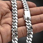 A close-up of a silver Cuban link chain bracelet being held in a person's hand, showing the polished metal links and clasp.