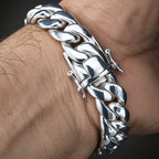 A close-up of a polished silver Cuban link bracelet worn on a person's wrist, showing the detailed curb links and clasp.