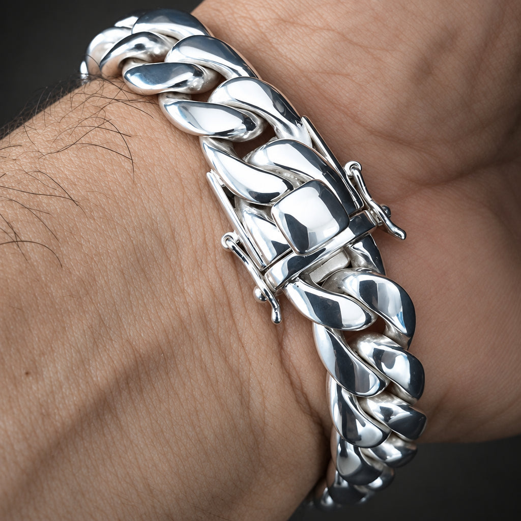 A close-up of a polished silver Cuban link bracelet worn on a person's wrist, showing the detailed curb links and clasp.