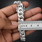 Silver bracelet being measured with a ruler against a dark background