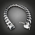 A polished silver Cuban link chain bracelet with a square clasp, displayed on a rustic wood slice against a solid black background.