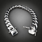 A polished silver Cuban link chain bracelet with a square clasp, displayed on a rustic wood slice against a solid black background.