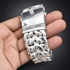 Silver bracelet with intricate design held in a hand against a dark background