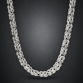 A silver-toned interlocking chain necklace with a braided or woven link design, shown draped against a dark gray gradient background.