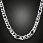 A close-up of a polished silver-tone Cuban link chain necklace arranged in a U-shape against a dark gray gradient background.