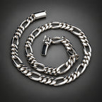 A polished silver-tone metal chain necklace with a curb-style link pattern, coiled on a dark gray gradient background.