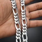 Silver chain held between fingers on a dark background
