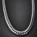 A close-up of a polished silver-tone Cuban link chain necklace arranged in a U-shape against a dark gray background.