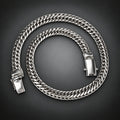 A thick silver-toned Cuban link chain necklace coiled on a dark gray gradient background.
