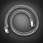 A thick silver-toned Cuban link chain necklace coiled on a dark gray gradient background.