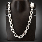 A polished silver-tone metal link chain necklace displayed on a black mannequin bust against a dark gray background.