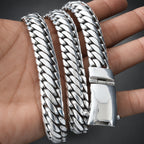A close-up of a polished silver-toned metal bracelet with a thick, textured rope chain link design, coiled on a person's hand.