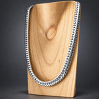 A thick silver Cuban link chain necklace displayed on a light wood neck stand against a dark gray studio background.
