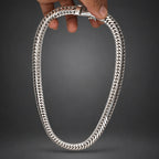 Silver chain necklace held by a hand on a dark gray background