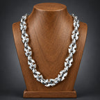 A chunky silver-toned metal chain necklace displayed on a polished wooden bust against a dark gray gradient background.