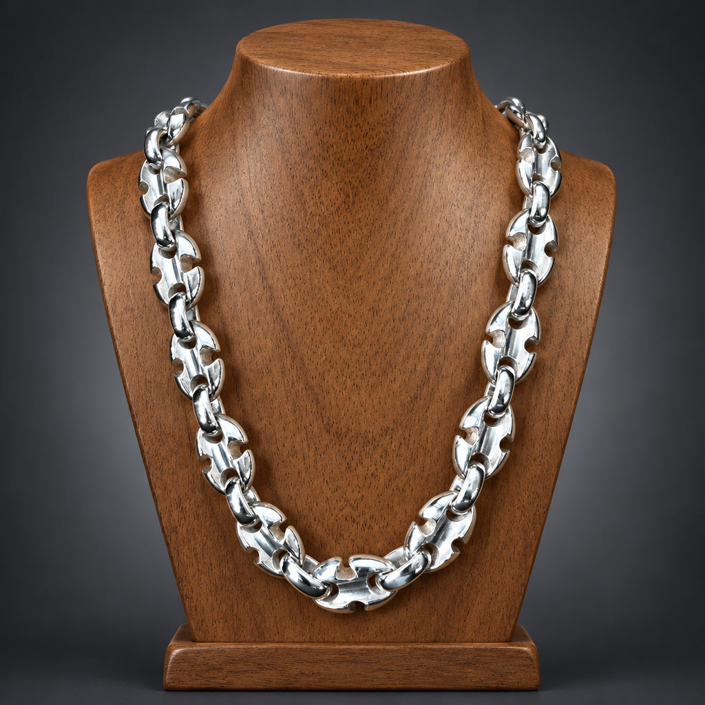 A chunky silver-toned metal chain necklace displayed on a polished wooden bust against a dark gray gradient background.
