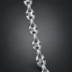 A close-up of a polished silver-toned metal chain with distinctive cutout links, shown against a dark gray gradient background.