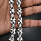Silver chain held between fingers on a dark background