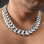 A close-up of a man wearing a thick, shiny silver Cuban link chain necklace.