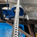 Close-up of a metal blade with teeth, held by a blue vise on a workshop bench.
