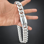 Silver chain bracelet being held by a hand on a dark surface