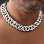 A close-up of a silver-toned Cuban link chain necklace worn around a man's neck.