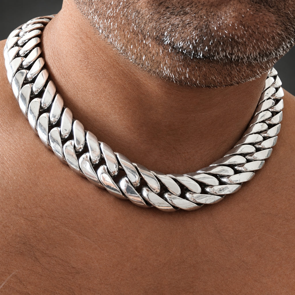 A close-up of a silver-toned Cuban link chain necklace worn around a man's neck.