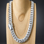 A thick silver Cuban link chain necklace displayed on a light wood neck stand against a dark gray background.