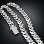 A close-up of a polished silver Cuban link chain necklace with a flat rectangular clasp, arranged on a dark black background.