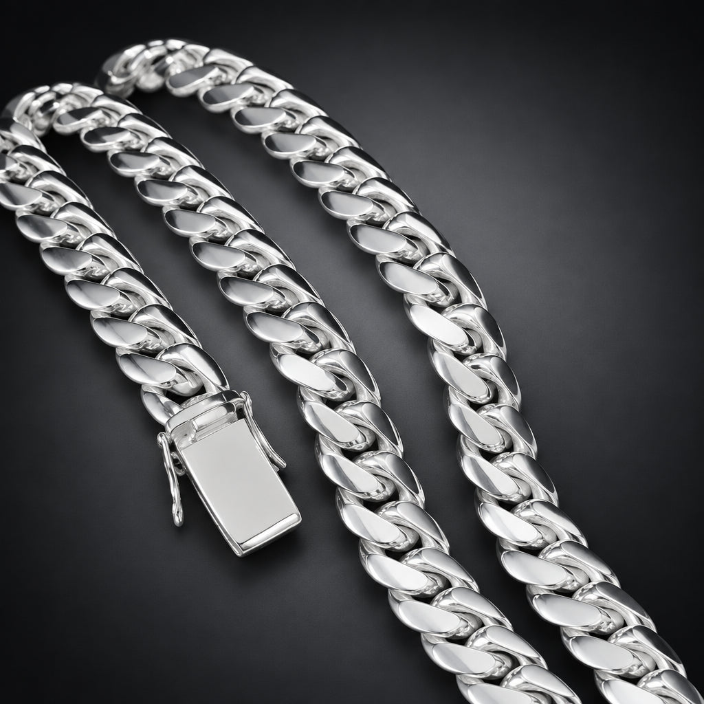 A close-up of a polished silver Cuban link chain necklace with a flat rectangular clasp, arranged on a dark black background.
