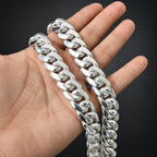 A close-up of a hand holding a thick, shiny silver Cuban link chain against a dark gray background.