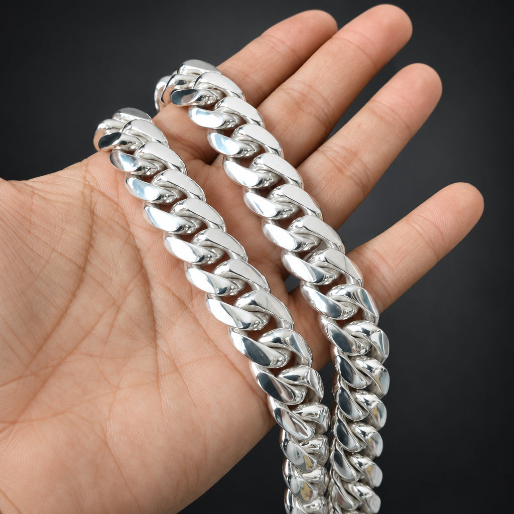 A close-up of a hand holding a thick, shiny silver Cuban link chain against a dark gray background.