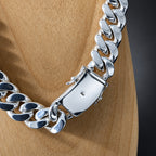 A close-up of a shiny silver Cuban link chain necklace displayed on a light wood mannequin torso against a dark gray background.
