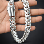 A polished silver Cuban link chain necklace draped over a person's hand against a dark background.