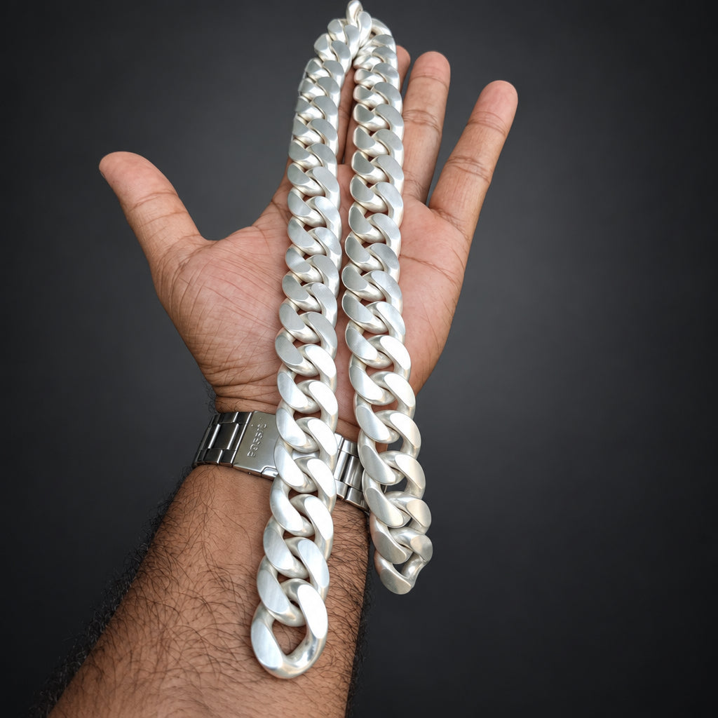 A thick silver Cuban link chain necklace draped over a person's hand against a dark gray background.