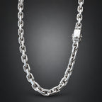 A polished silver-toned metal chain necklace with a rectangular clasp, shown draped against a dark gray gradient background.