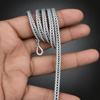Silver braided necklace held in a hand against a dark background
