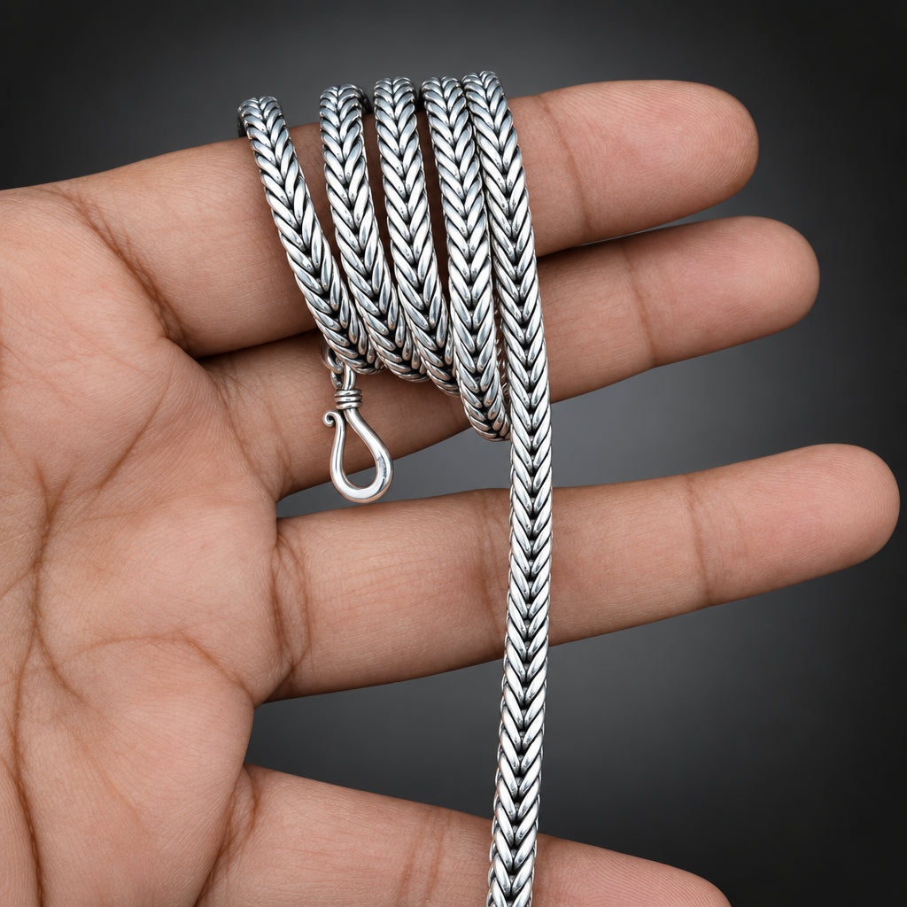 Silver braided necklace held in a hand against a dark background