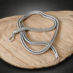 Silver braided necklace on a wooden surface with a dark background
