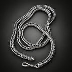 Silver braided necklace on a hand against a dark background