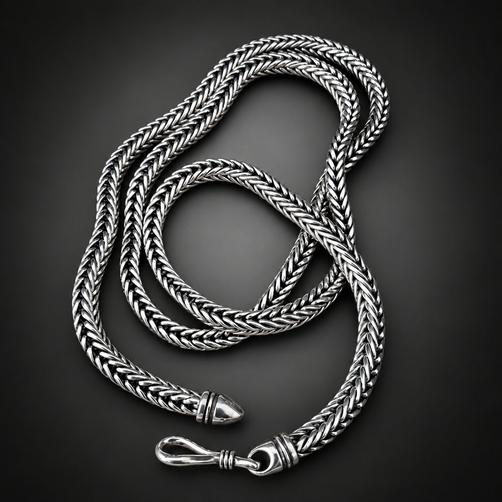 Silver braided necklace on a hand against a dark background