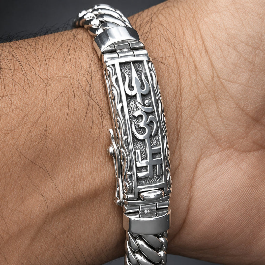 A close-up of a silver-toned metal bracelet with an Om symbol and intricate engravings, worn on a person's wrist.