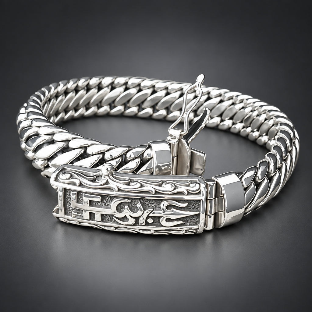 A silver-toned Cuban link chain bracelet with an ornate engraved clasp, displayed on a textured beige surface against a dark background.