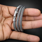 Two silver braided bracelets on a person's wrist against a dark background