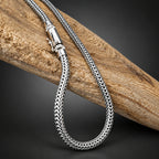 Silver braided necklace on a wooden log with a dark background