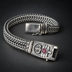 Silver bracelet with intricate design and red gemstone on a textured surface