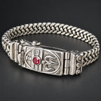 Silver bracelet with intricate design and red gemstone on a dark background