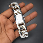 Silver bracelet held in a hand against a plain background