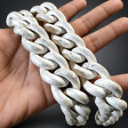 A close-up of a hand holding a thick, rustic white braided chain or rope against a natural rocky background.
