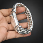 Silver bracelet held in a hand against a dark background